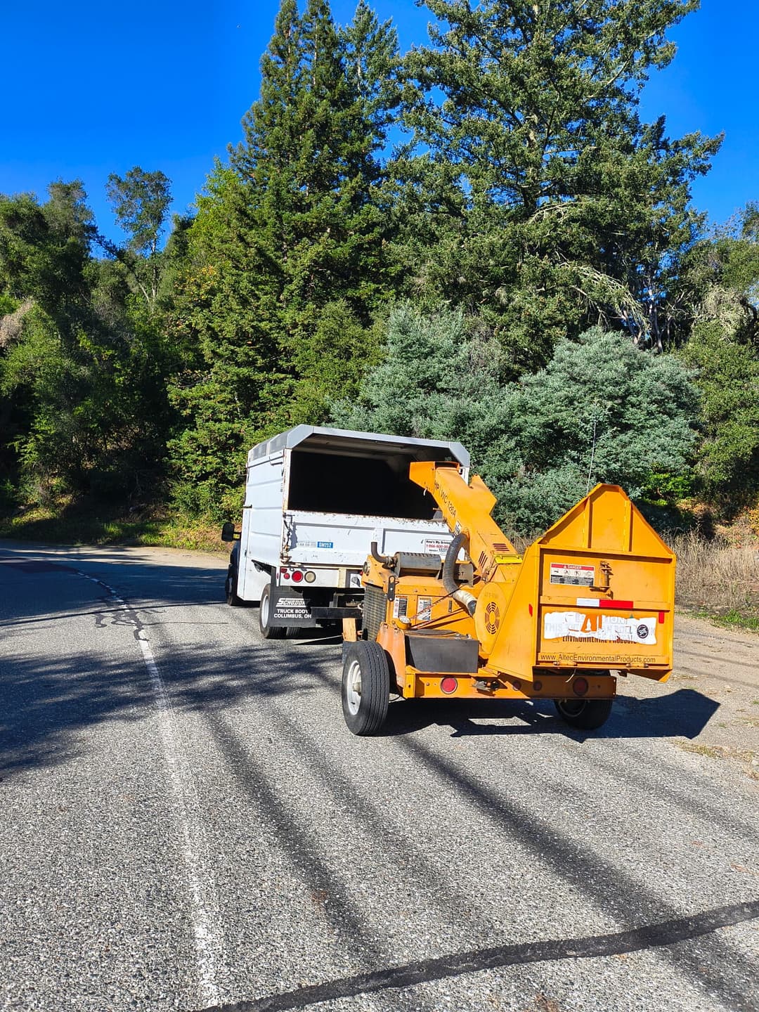 Mobile wood chipper parked behind a white work van on a forested roadside