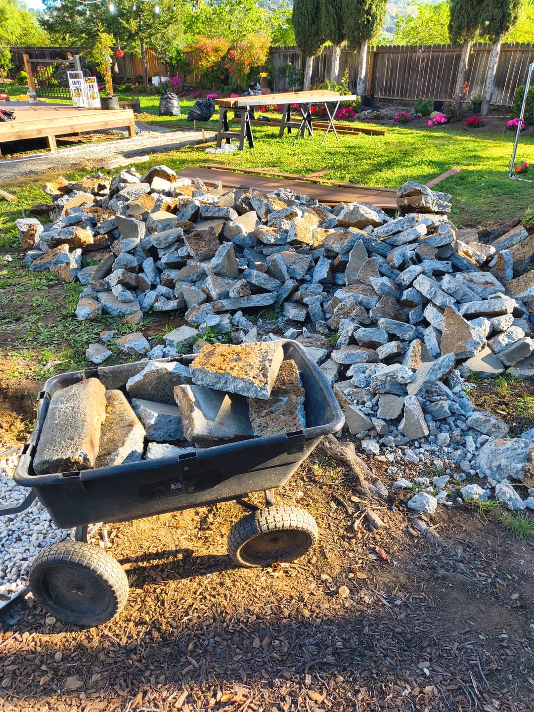 Pile of broken concrete chunks with wheelbarrow during concrete demolition and debris removal in backyard