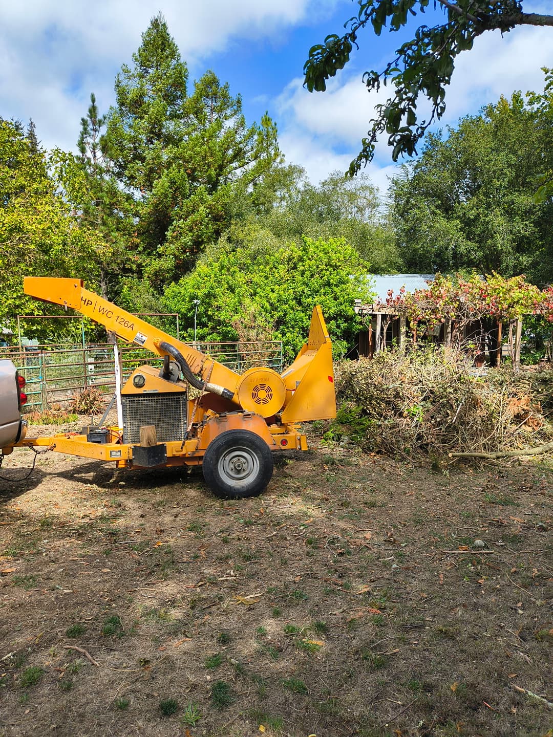 Orange wood chipper trailer parked at rural property during tree trimming and brush chipping service